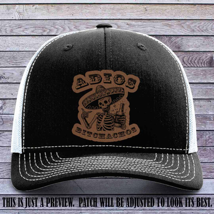 Dark brown leather patch on Black to White Richardson 112 trucker hat featuring “Adios Bitchachos” skeleton design.