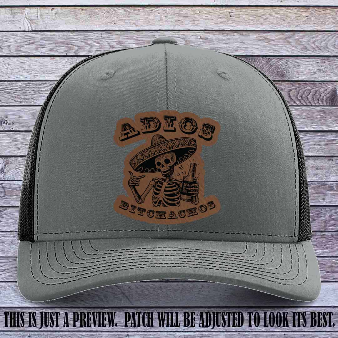 Dark brown leather patch on Heather Grey to Black Richardson 112 trucker hat featuring “Adios Bitchachos” skeleton design.