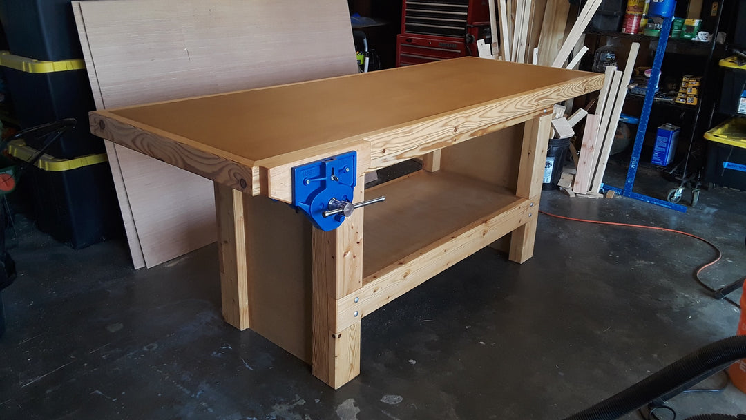 Wooden workbench with blue clamp in a cluttered garage workshop.