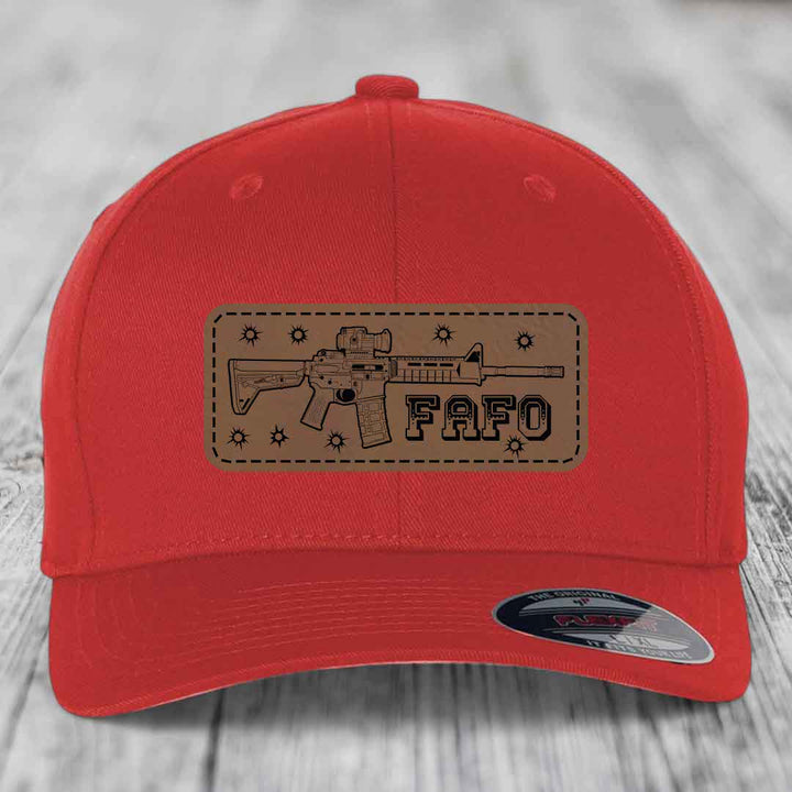 Red baseball cap with brown leather patch featuring AR-15 rifle graphic and &