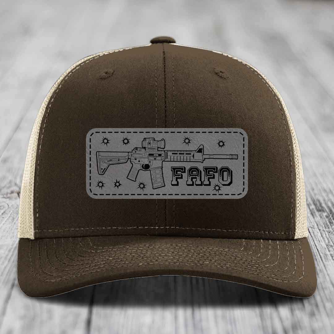 Brown trucker hat with grey leatherette patch featuring AR-15 rifle graphic and &