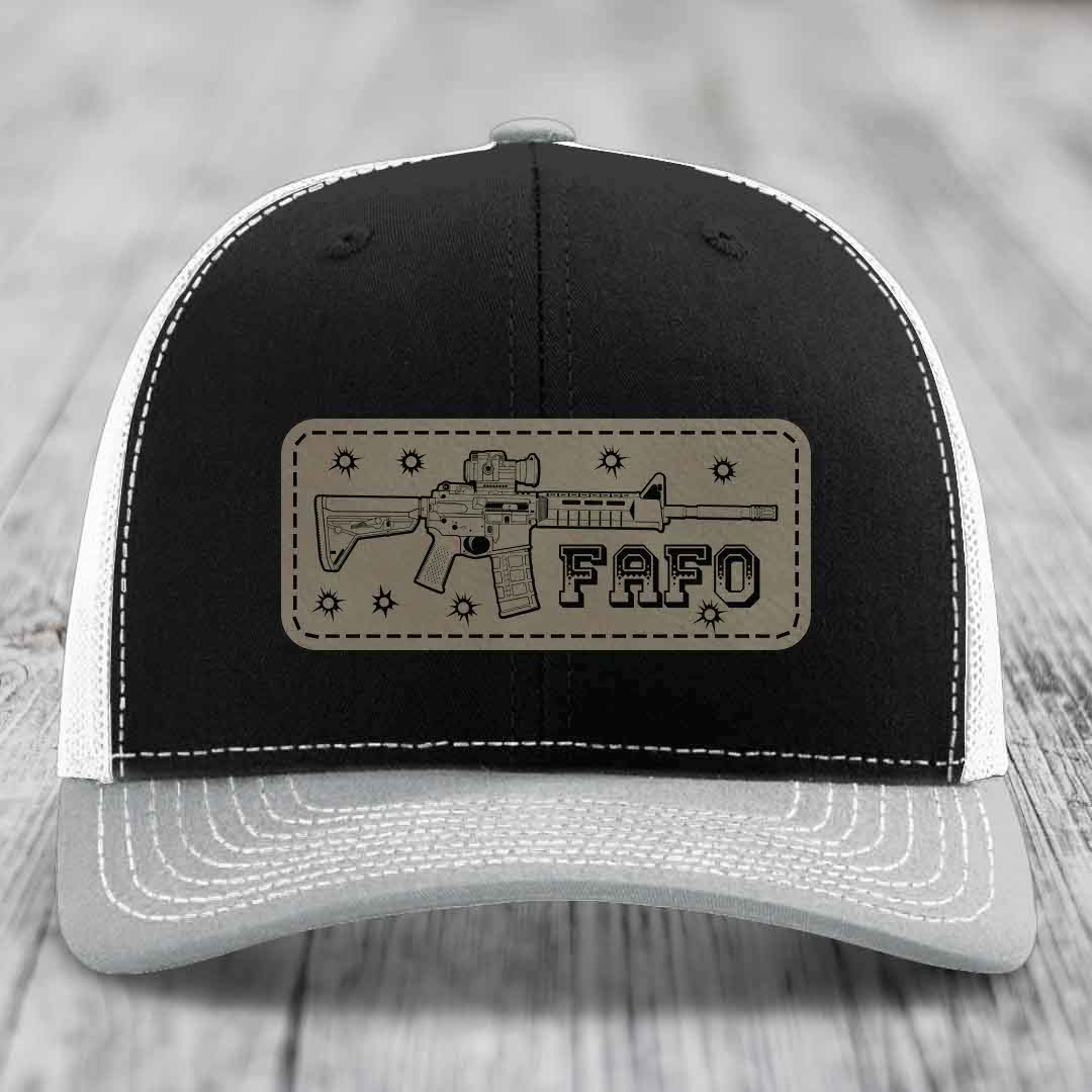 Black and white trucker hat with tan leather patch featuring AR-15 rifle graphic and &