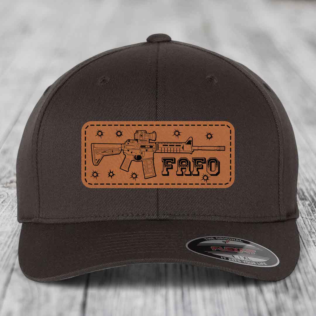 Dark brown baseball cap with tan leather patch featuring AR-15 rifle graphic and &