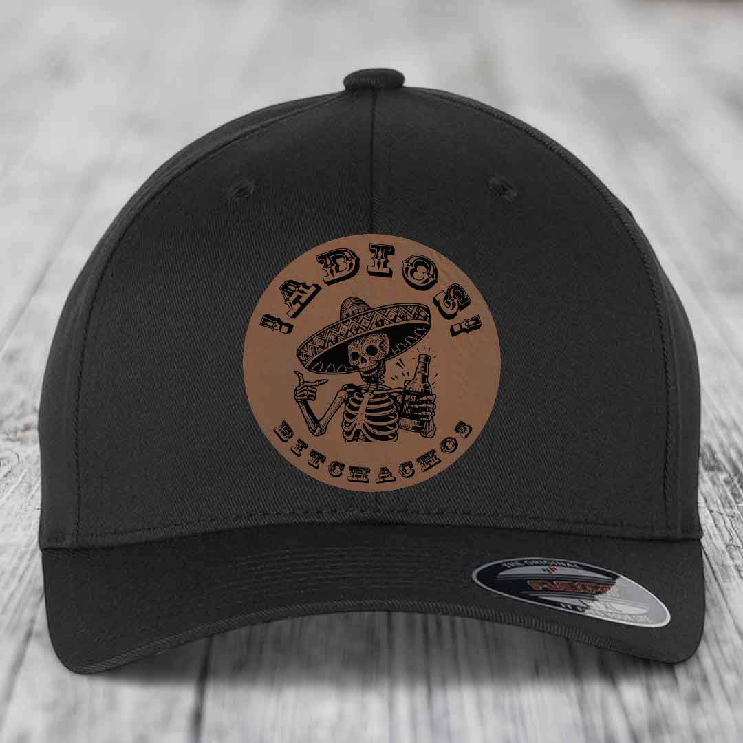 Black baseball cap with brown circular leather patch featuring skeleton in sombrero holding beer bottle and text &