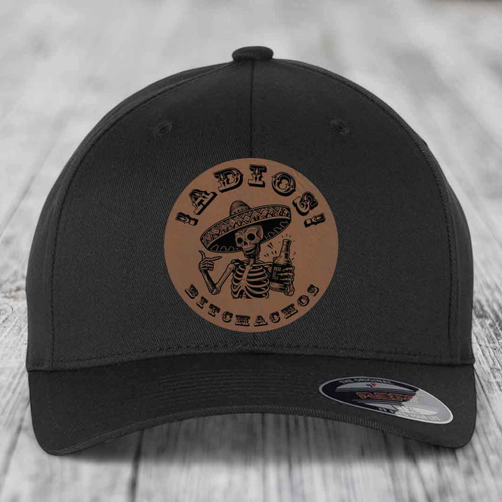 Black baseball cap with brown circular leather patch featuring skeleton in sombrero holding beer bottle and text &