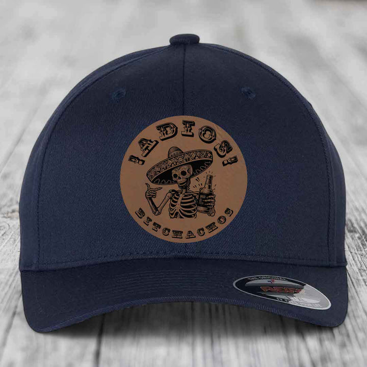 Dark blue baseball cap with a brown leather patch featuring a skeleton in a sombrero holding a beer bottle and the text &