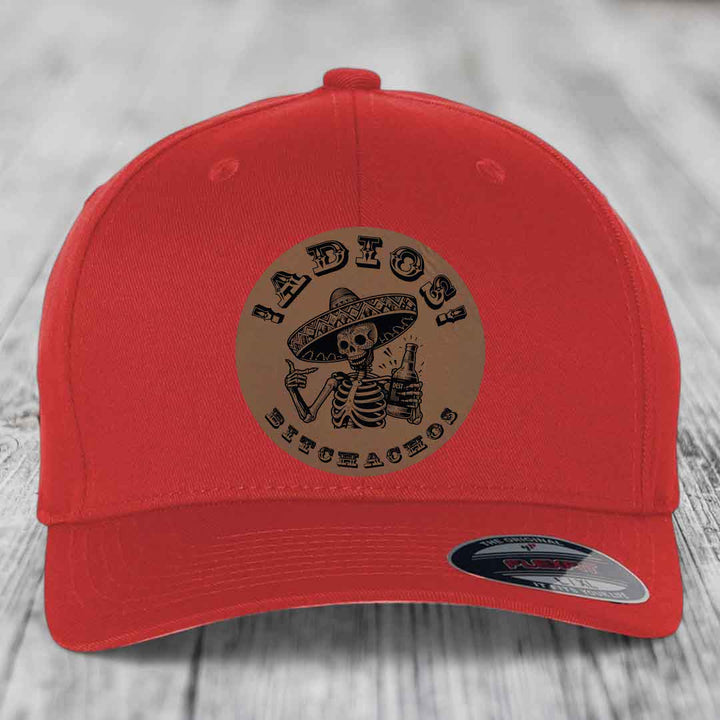 Red baseball cap with circular brown patch featuring skeleton in sombrero holding beer bottle and text &