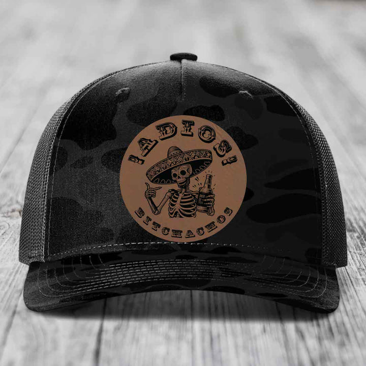Black camouflage trucker hat with a brown leather patch featuring a skeleton in a sombrero holding a beer bottle.