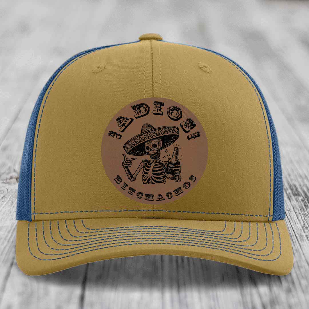 Tan and blue trucker hat with a circular leather patch featuring a skeleton in a sombrero holding a beer bottle.