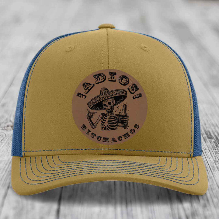 Tan and blue trucker hat with a circular leather patch featuring a skeleton in a sombrero holding a beer bottle.
