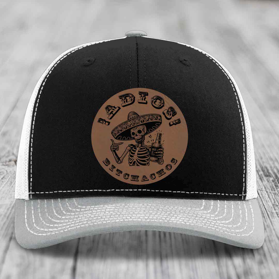 Black and grey trucker hat with a brown leather patch featuring a skeleton in a sombrero holding a beer bottle.
