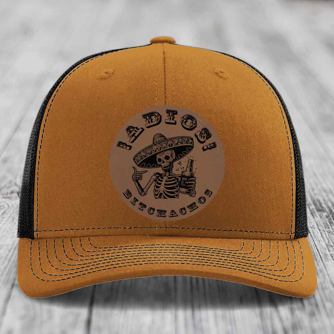 Tan trucker hat with black mesh back and embroidered skull holding beer bottle patch.