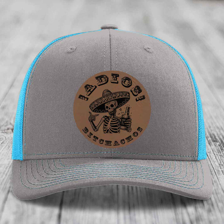Grey trucker hat with blue mesh back and brown leather patch featuring a skeleton in a sombrero holding a beer bottle.