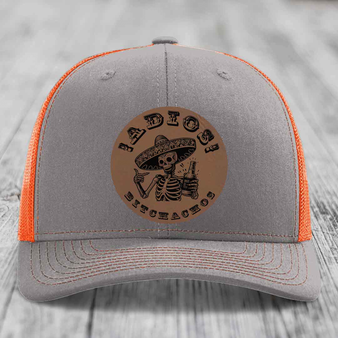 Grey trucker hat with orange mesh back and a brown leather patch featuring a skeleton in a sombrero holding a beer bottle.