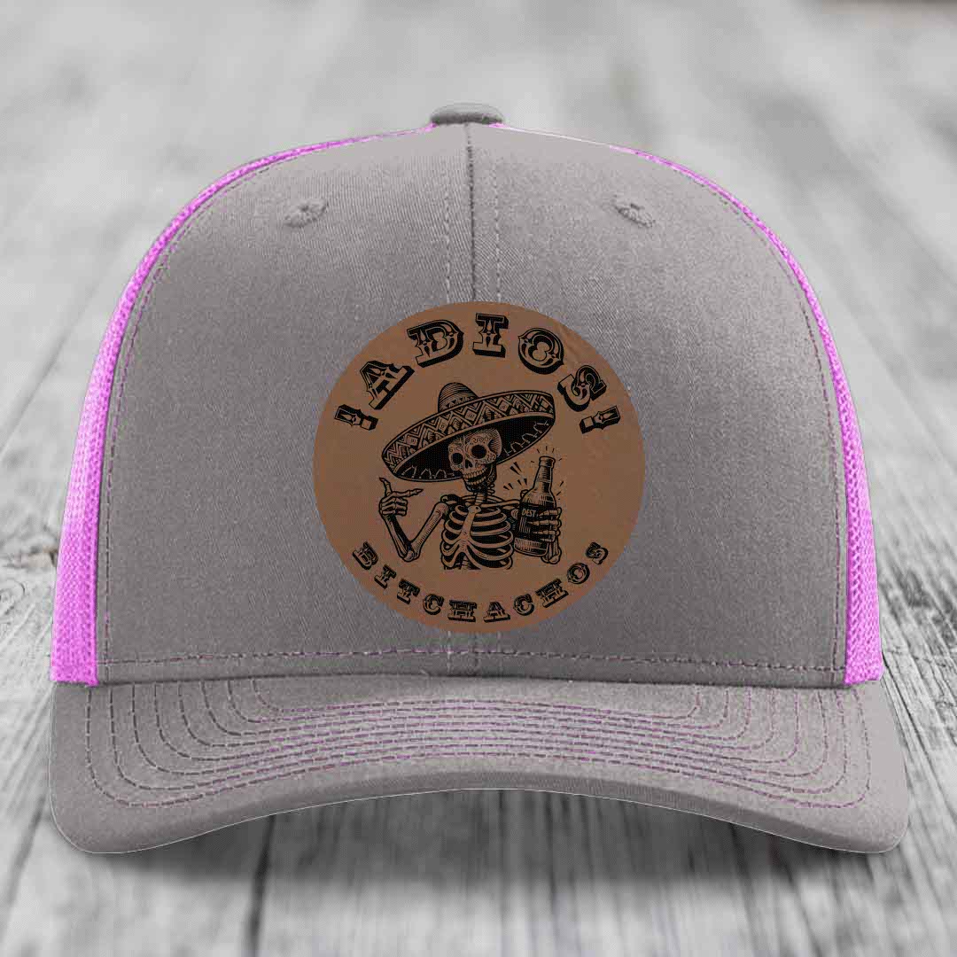Grey trucker hat with pink mesh and a brown leather patch featuring a skeleton in a sombrero holding a beer bottle.