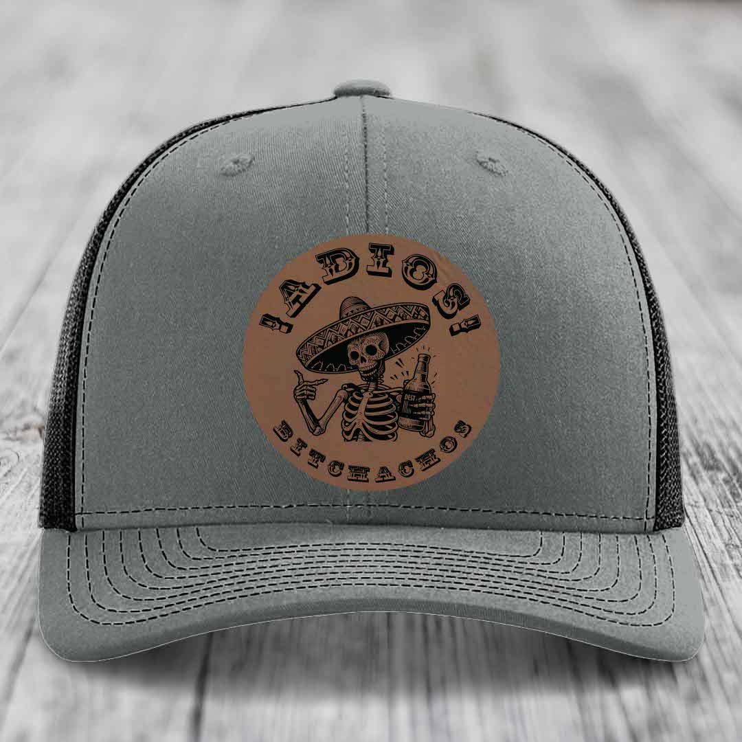 Grey trucker hat with brown leather patch featuring skeleton in sombrero holding beer bottle.