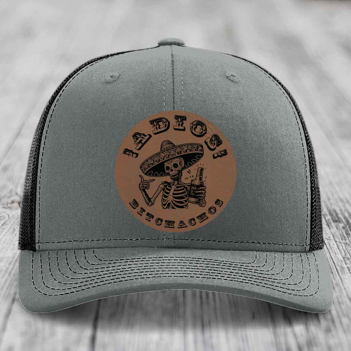 Grey trucker hat with brown leather patch featuring skeleton in sombrero holding beer bottle.