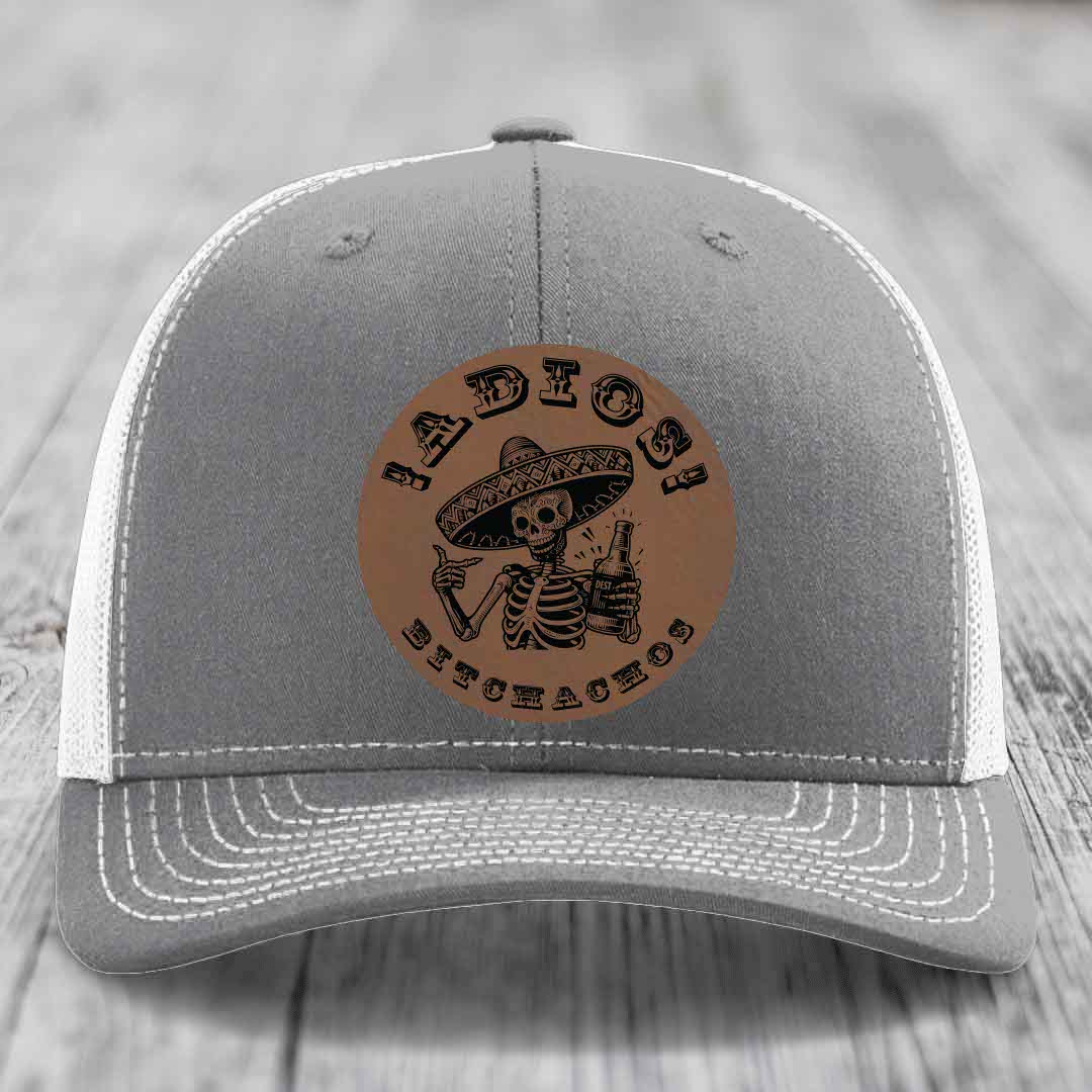 Grey trucker hat with brown leather patch featuring skeleton in sombrero holding beer bottle and text &