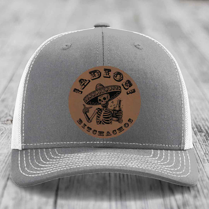 Grey trucker hat with brown leather patch featuring skeleton in sombrero holding beer bottle and text &
