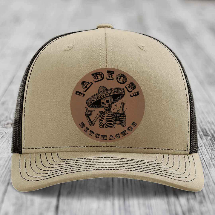 Beige trucker hat with brown leather patch featuring skeleton in sombrero holding beer bottle and text &