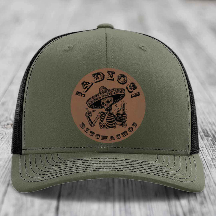 Olive green trucker hat with brown leather patch featuring skeleton in sombrero holding bottle and text &