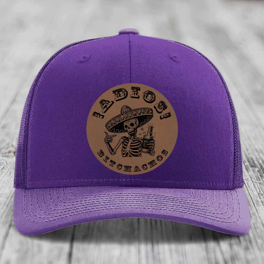 Purple trucker hat with brown circular patch featuring a skeleton in a sombrero holding a beer bottle and the text &