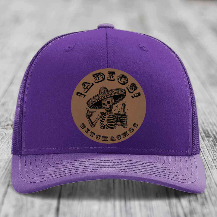 Purple trucker hat with brown circular patch featuring a skeleton in a sombrero holding a beer bottle and the text &