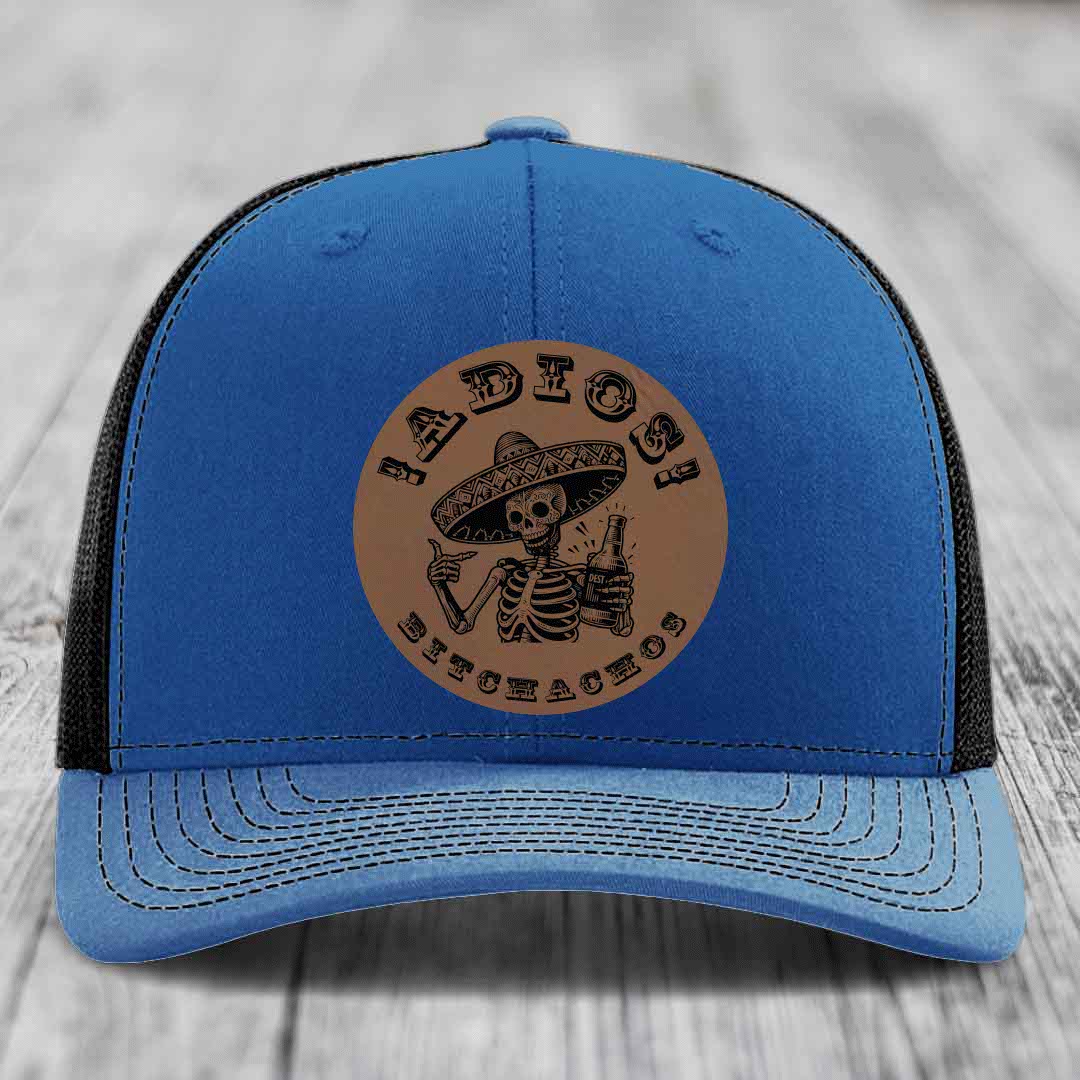 Blue trucker hat with brown leather patch featuring skeleton in sombrero holding bottle and text &
