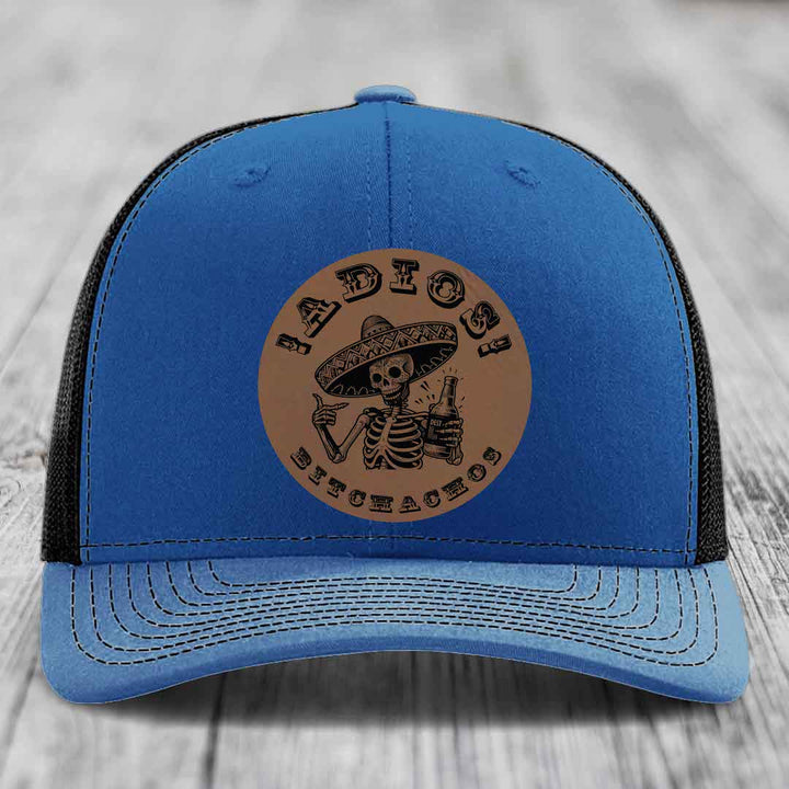 Blue trucker hat with brown leather patch featuring skeleton in sombrero holding bottle and text &