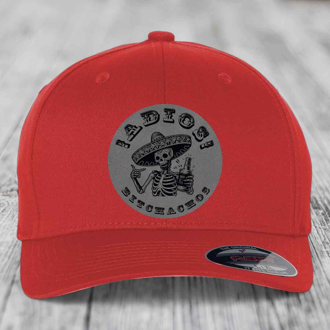Red baseball cap with grey circular patch featuring skeleton in sombrero holding beer bottle and text &