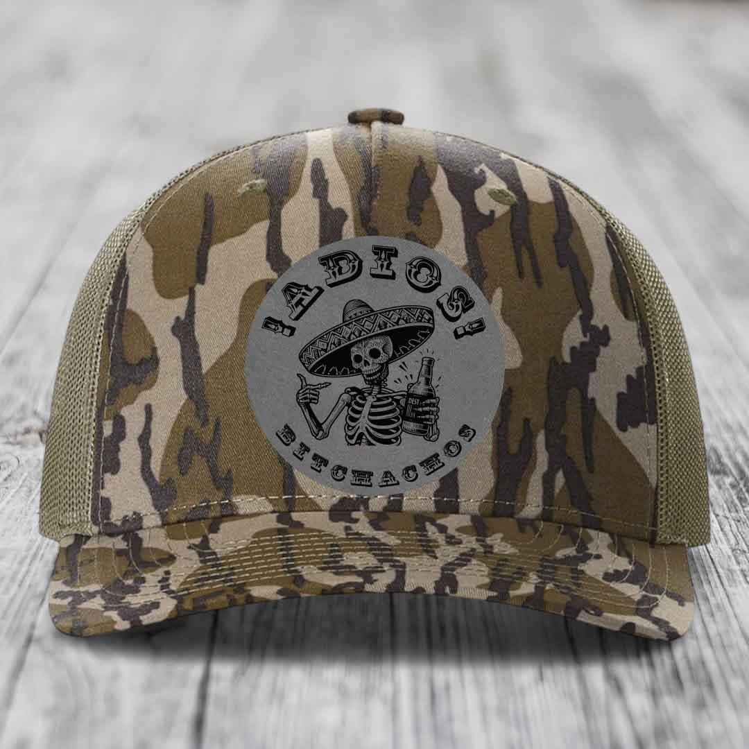 Camouflage trucker hat with grey circular patch featuring skeleton in sombrero holding beer bottle and text &