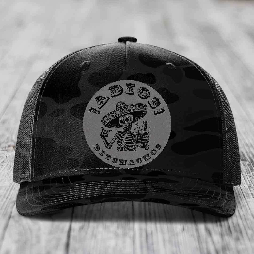 Black camouflage trucker hat with a circular patch featuring a skeleton in a sombrero holding a beer bottle and the text &