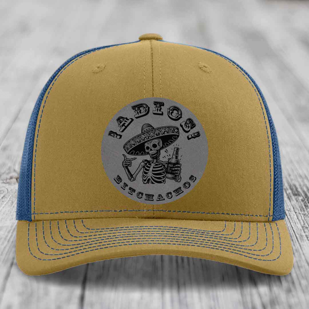 Tan and blue trucker hat with a circular grey patch featuring a skeleton in a sombrero holding a beer bottle and the text &