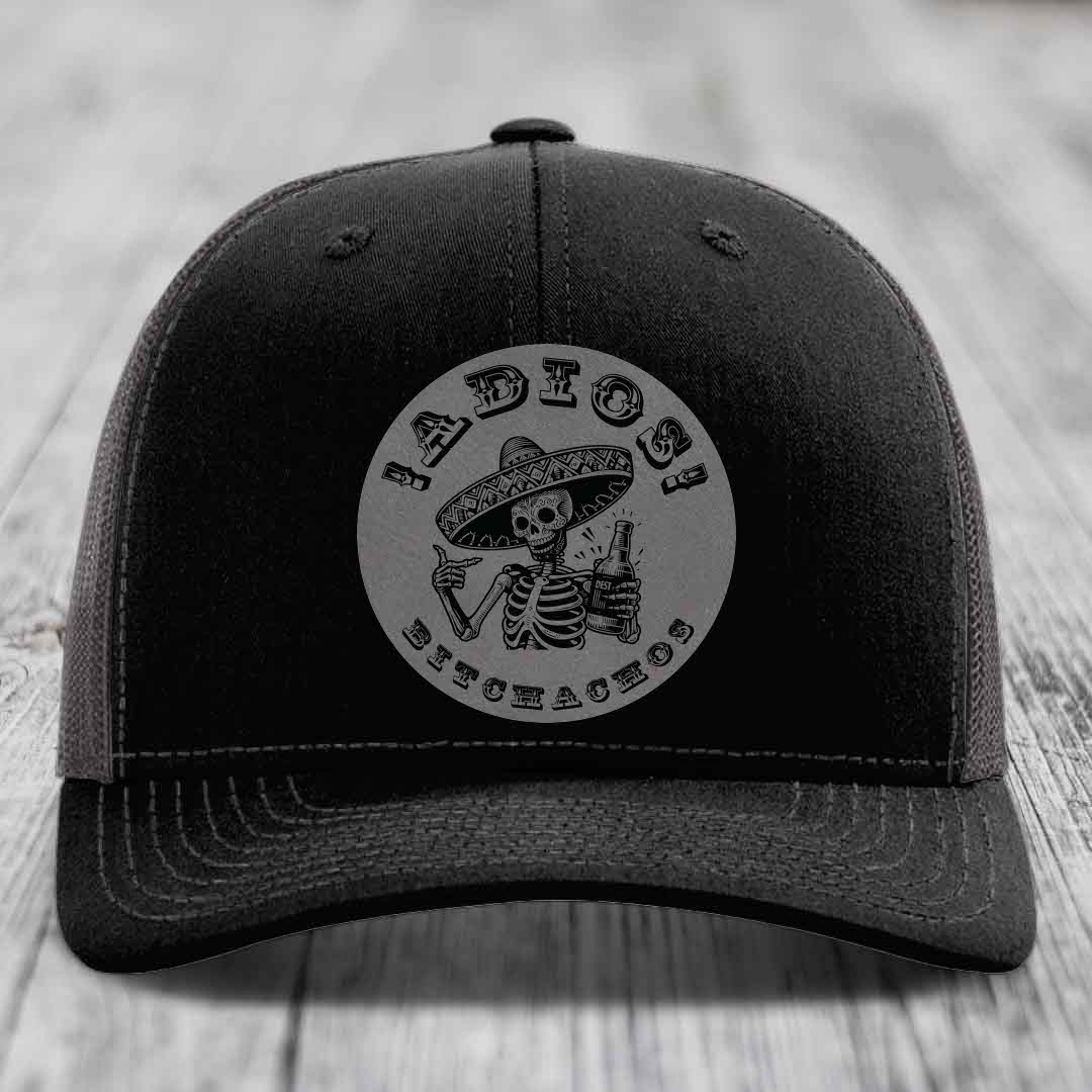 Black trucker hat with grey circular patch of skeleton in sombrero holding beer bottle and text &