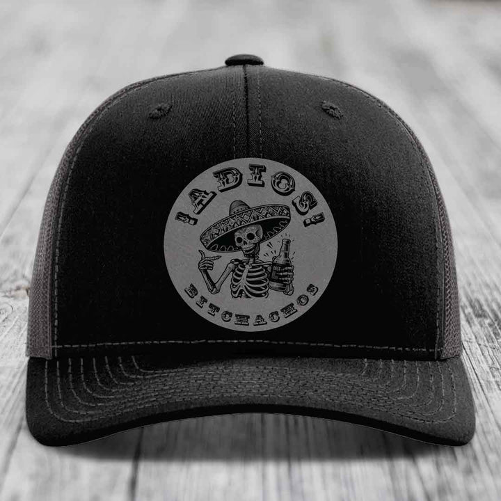 Black trucker hat with grey circular patch of skeleton in sombrero holding beer bottle and text &