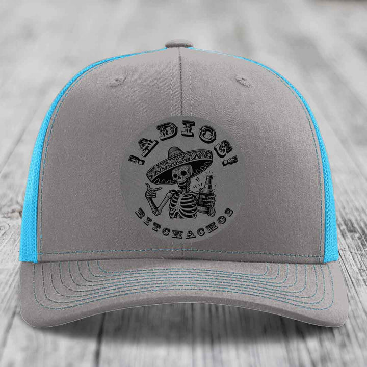 Grey trucker hat with blue mesh back and black skull patch reading &