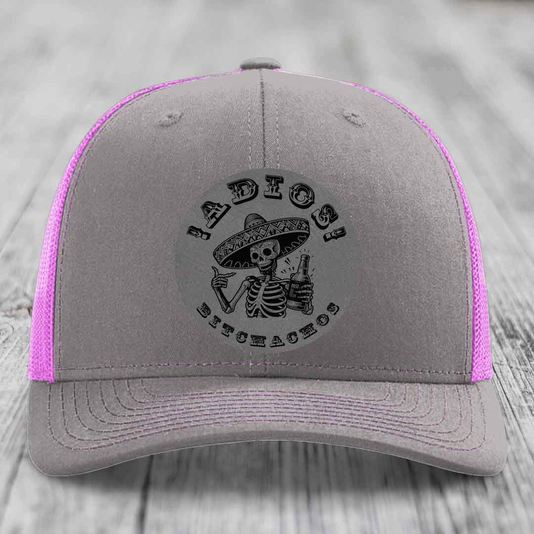 Grey trucker hat with pink mesh sides and a black skull-and-sombrero patch that says &