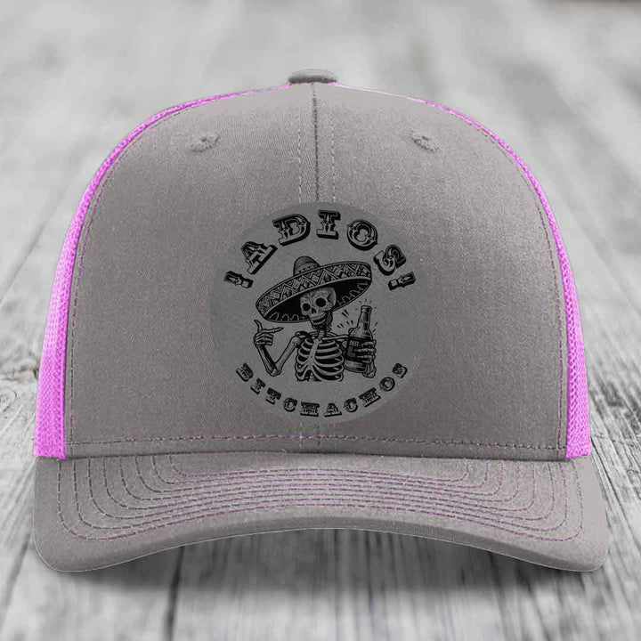 Grey trucker hat with pink mesh sides and a black skull-and-sombrero patch that says &
