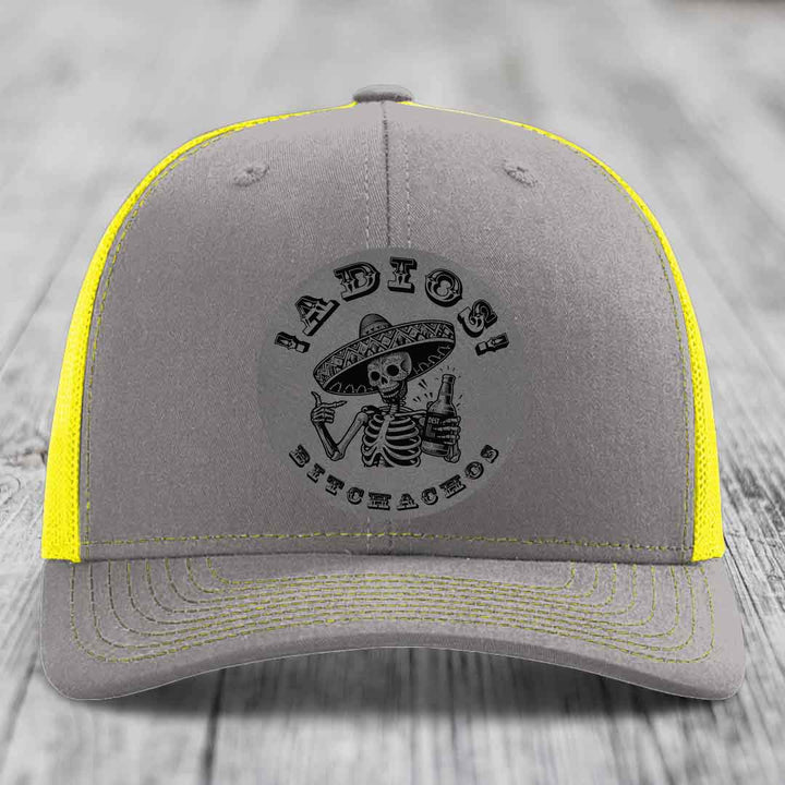 Grey trucker hat with yellow mesh and stitching, featuring a black skull-and-sombrero patch that reads &