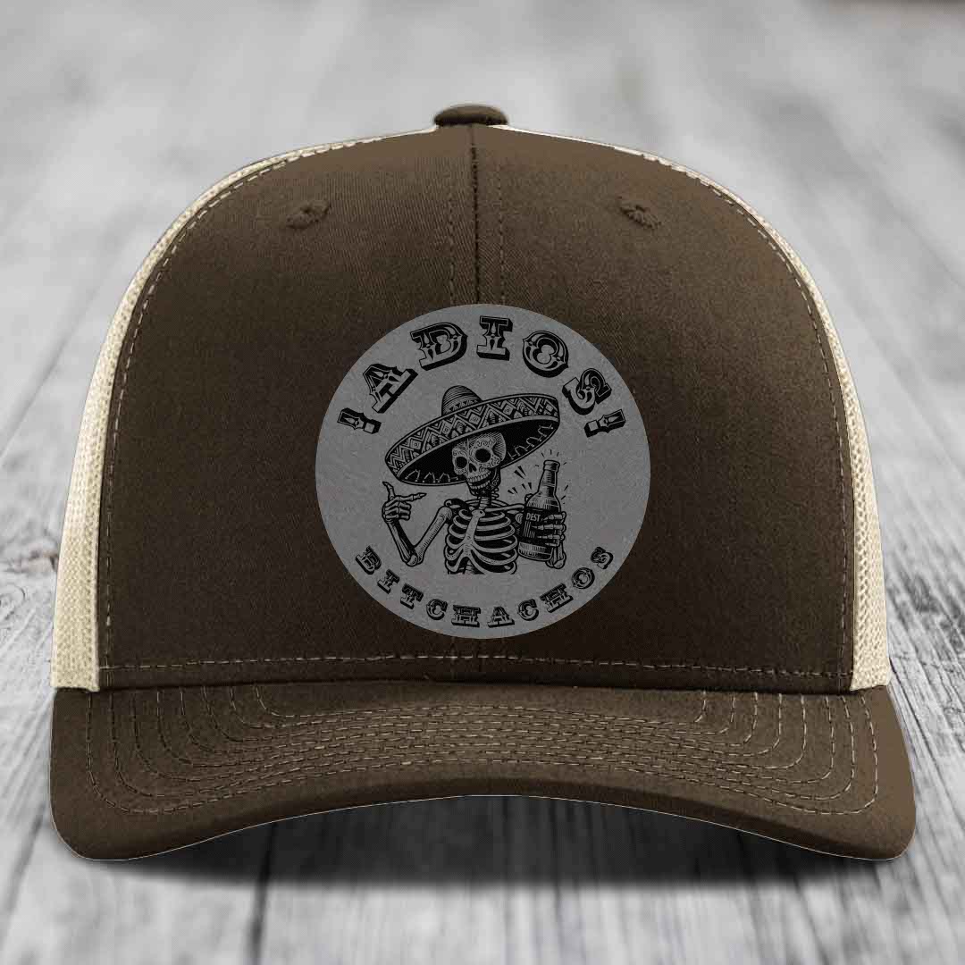 Brown trucker hat with beige mesh back and gray circular patch featuring a skeleton in a sombrero holding a beer bottle.