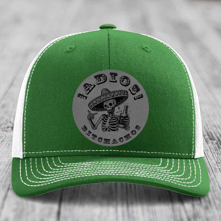 Green trucker hat with white mesh back and stitching, featuring a circular grey patch with a skeleton in a sombrero holding a beer bottle and text &