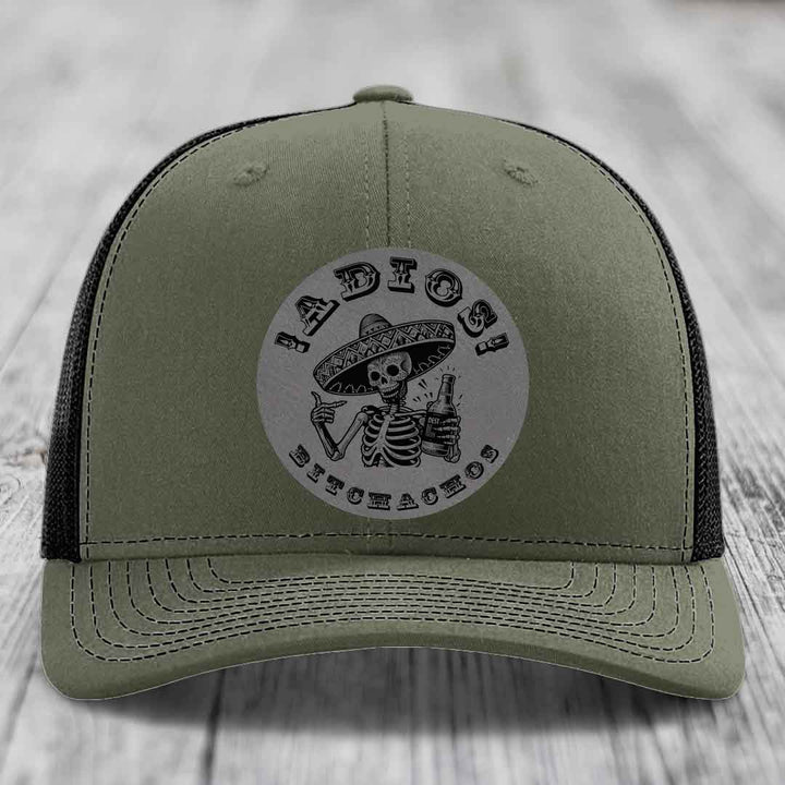 Olive green trucker hat with black mesh back and a circular grey patch featuring a skeleton in a sombrero holding a beer bottle, with the text &