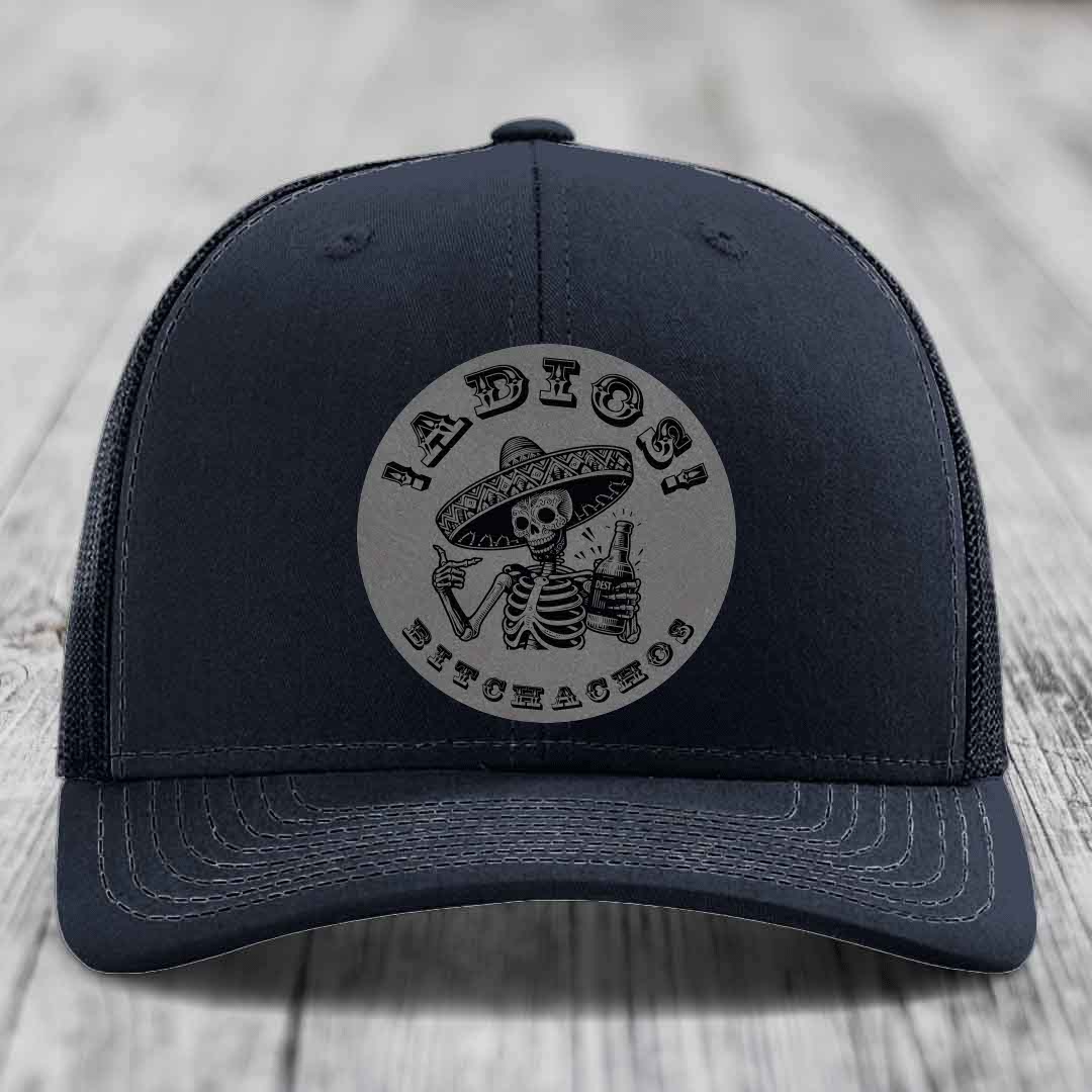 Black trucker hat with grey circular patch featuring skeleton in sombrero holding beer bottle and text &