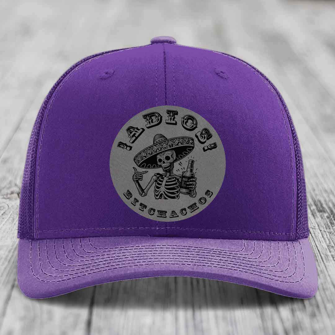 Purple trucker hat with grey circular patch featuring a skeleton in a sombrero holding a beer bottle and the text &