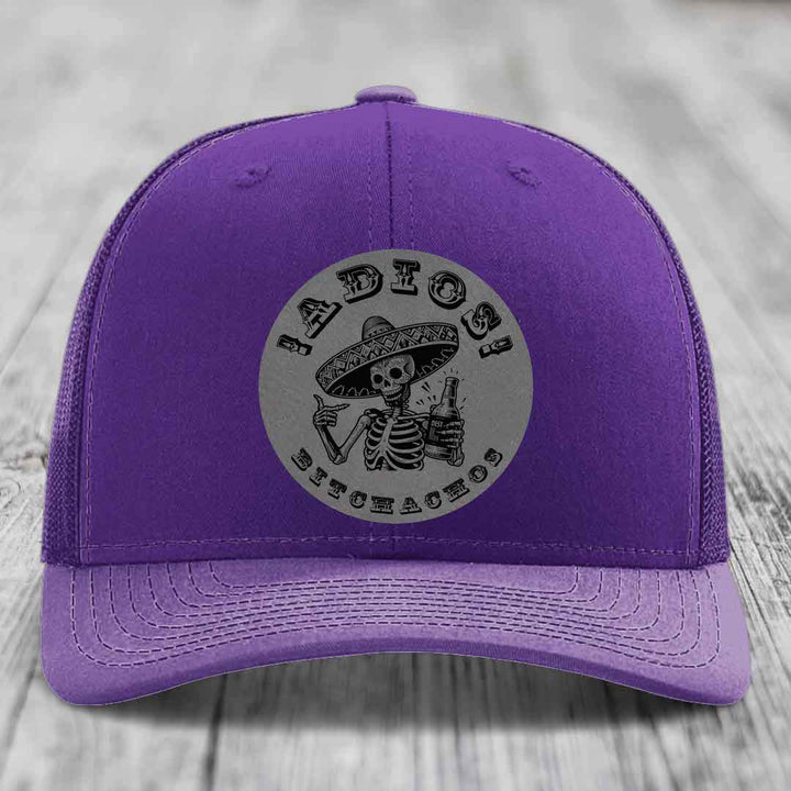 Purple trucker hat with grey circular patch featuring a skeleton in a sombrero holding a beer bottle and the text &