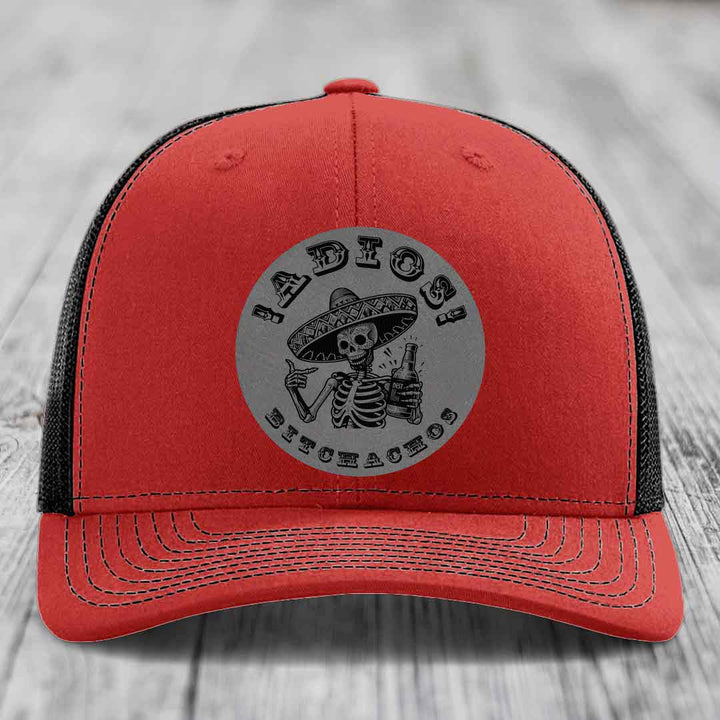 Red trucker hat with black mesh back and gray circular patch featuring a skeleton in a sombrero holding a beer bottle with text &