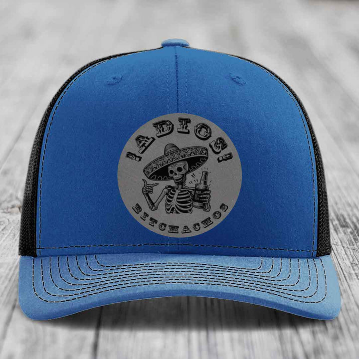 Blue trucker hat with black mesh back and gray circular patch featuring a skeleton in a sombrero holding a beer bottle with text &