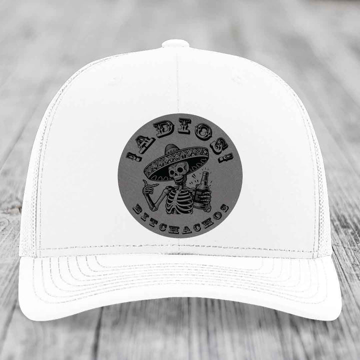 White trucker hat with black circular patch featuring skeleton in sombrero holding beer bottle and text &