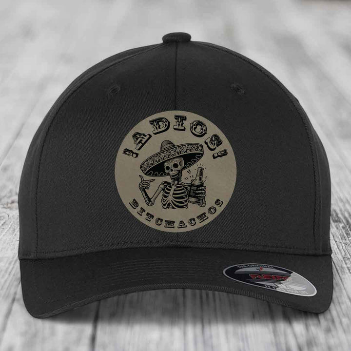 Black baseball cap with circular beige patch featuring skeleton in sombrero holding beer and text &
