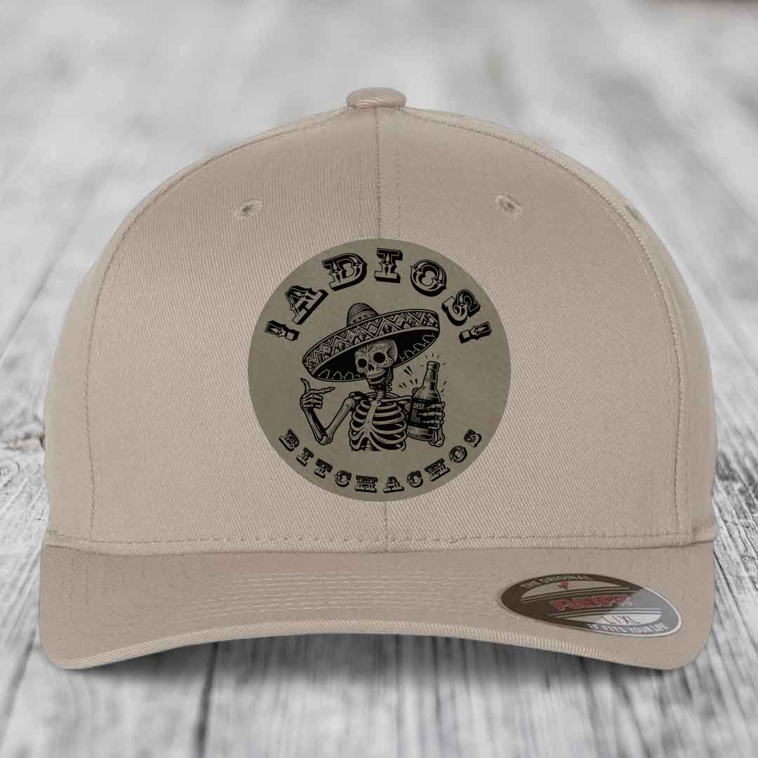 Beige baseball cap with circular patch featuring skeleton in sombrero holding beer, text &